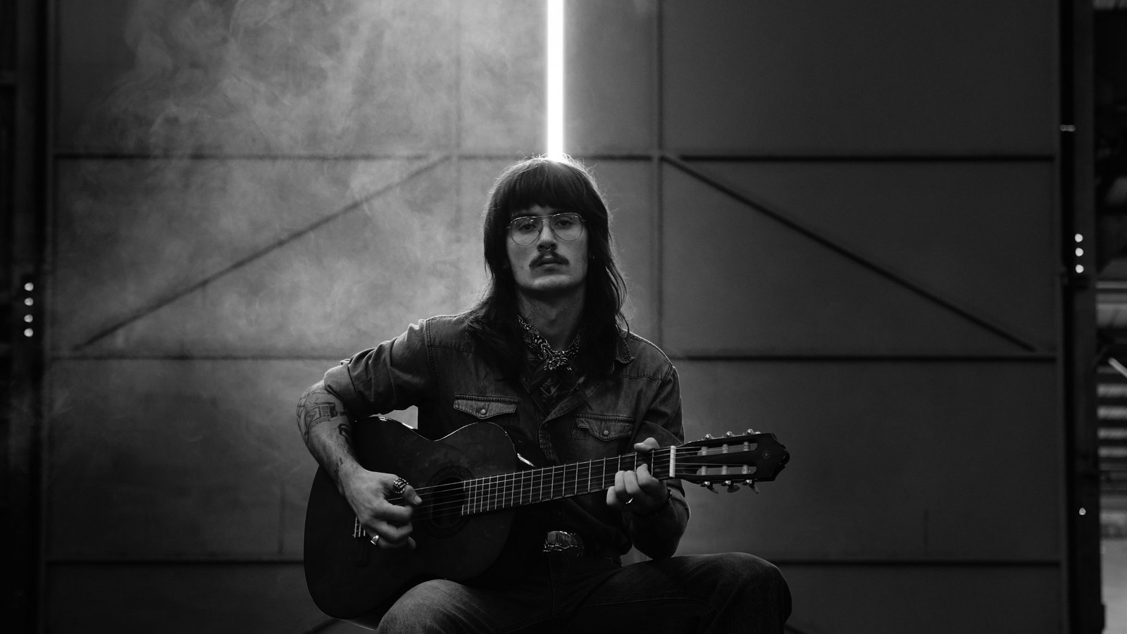 Wren Hollis seated with a parlor guitar under a strip light